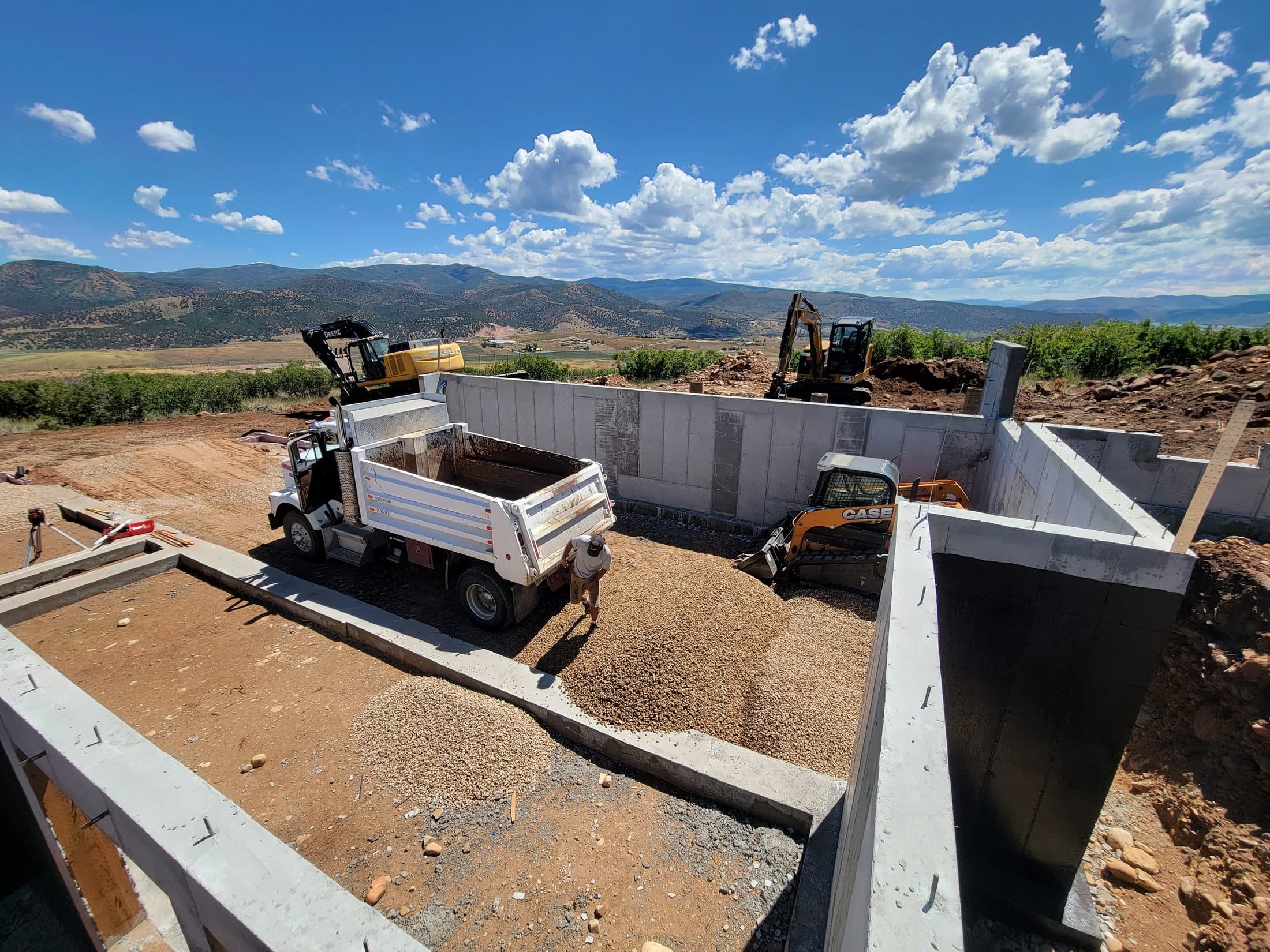 Excavators and a dump truck working around a concrete foundation.
