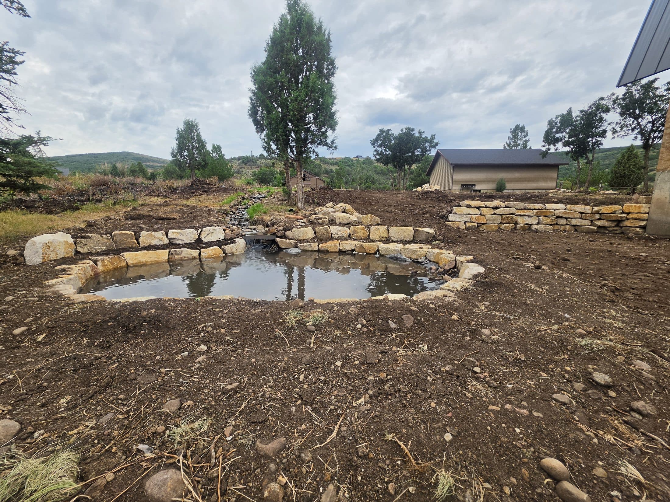 Rock-lined pond and small water channel on a graded property.